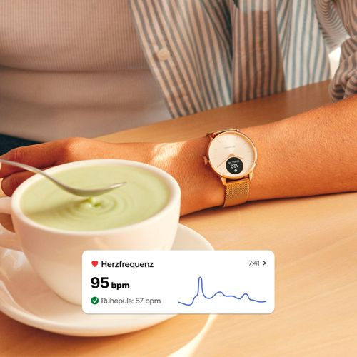 Eine Person trägt eine goldene Smartwatch und rührt in einer grünen Tasse.