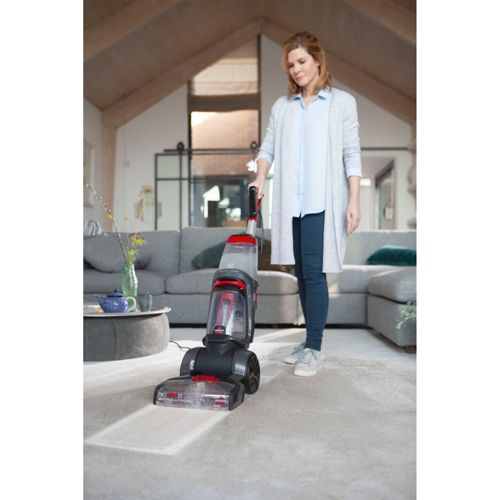 Eine Frau benutzt einen roten und grauen Teppichreiniger in einem Wohnzimmer.