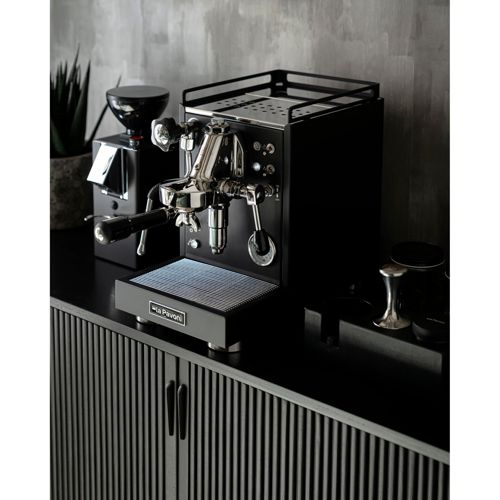 Schwarze Espressomaschine mit Chromdetails, daneben eine Kaffeemühle auf einem Schrank.