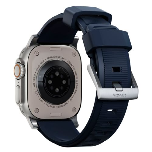 Parte trasera de un reloj inteligente plateado con correa azul marino. Texto: 'WATCH ULTRA'.