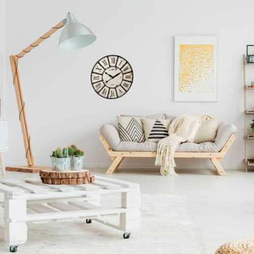 Ein Wohnzimmer mit einer Holzstehlampe, einer Uhr, einem Sofa mit Kissen und einem weißen Paletten-Couchtisch.