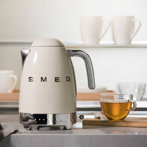 Een crèmekleurige SMEG waterkoker staat op een aanrecht naast een glazen kop thee.