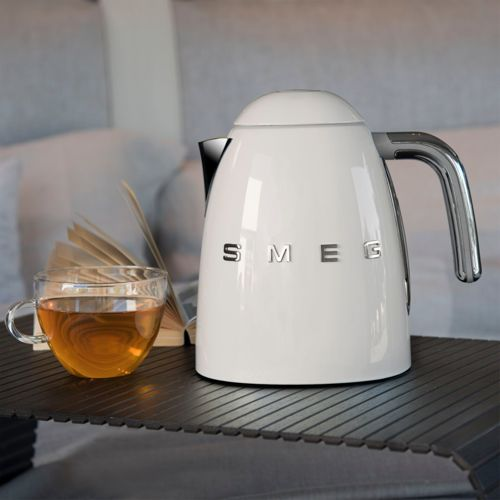 Een witte Smeg waterkoker naast een kop thee en een open boek.