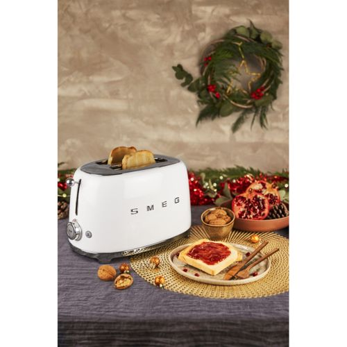 Biały toster SMEG z tostami, obok tost z dżemem i owocami.