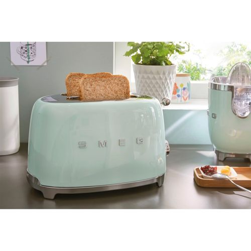 Ein hellgrüner SMEG-Toaster mit zwei Scheiben Toastbrot, daneben ein Entsafter.