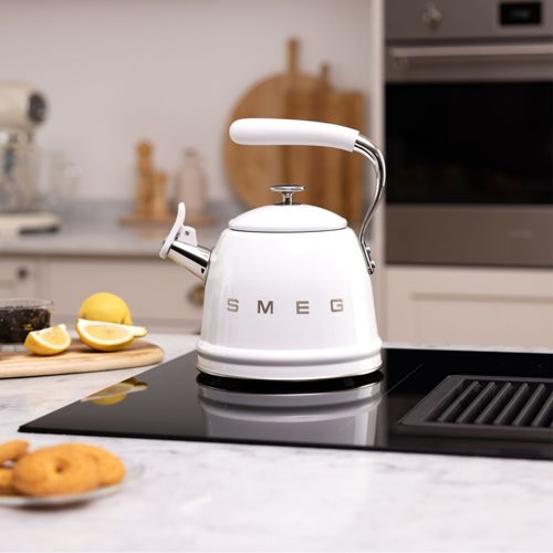 Eine weiße SMEG-Teekanne steht auf einem Induktionskochfeld mit Zitronenscheiben daneben.