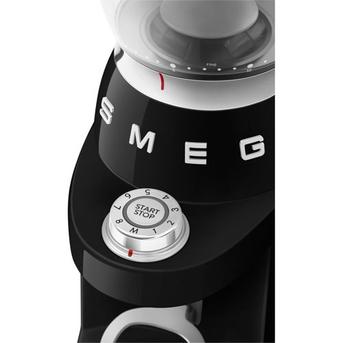Primer plano de un molinillo de café SMEG negro con dial plateado START/STOP y números.