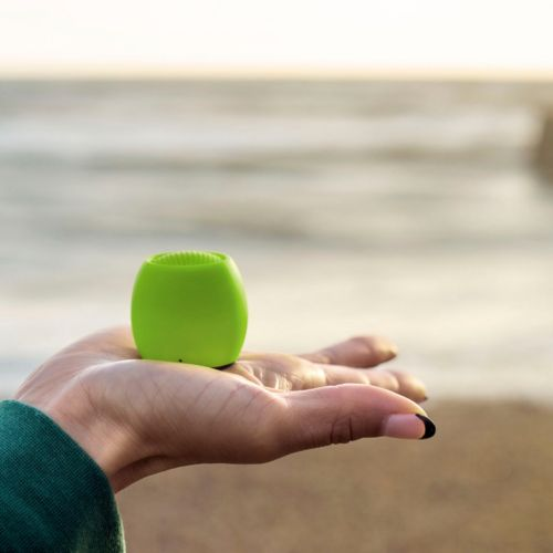Zielona szczoteczka spoczywa na dłoni na plaży, z morzem w tle.
