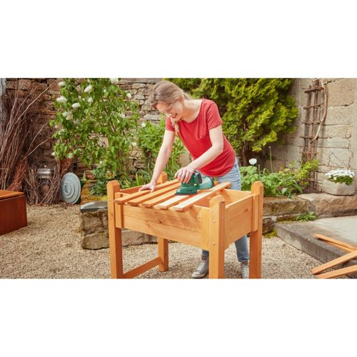 Frau schleift Holz für ein Hochbeet im Garten.