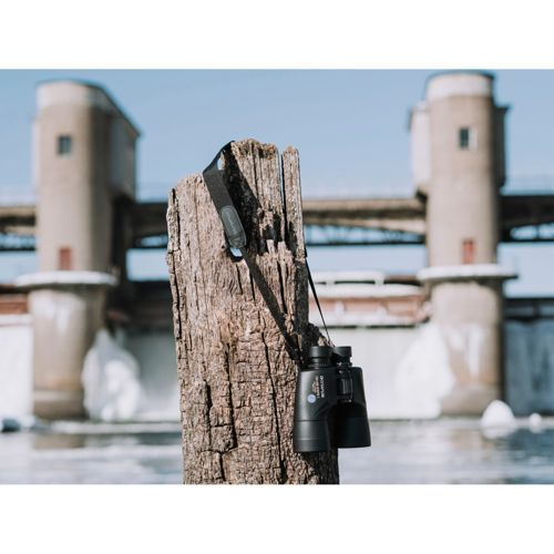 Schwarze Fernglas hängt an einem Holzpfahl vor einer Schleuse.
