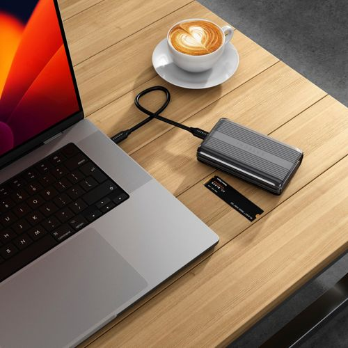 Un laptop, disco rigido esterno, SSD e tazza di caffè su tavolo in legno.