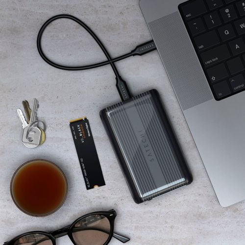 Un disco esterno, SSD, chiavi, occhiali e una tazza di caffè su una scrivania.
