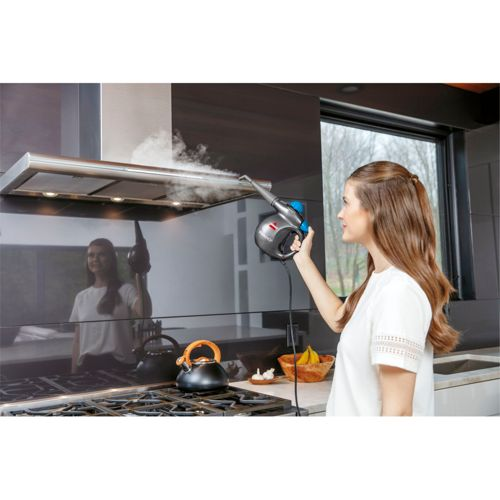 Una mujer usa un limpiador a vapor en la campana extractora de una cocina.