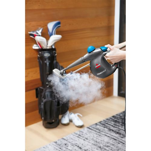 Un limpiador a vapor rocía vapor sobre una bolsa de golf junto a palos y zapatos.
