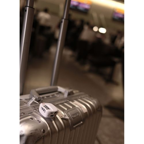 Una valigia argentata con lucchetto a combinazione bianco si trova in una sala d'aeroporto affollata e sfocata.