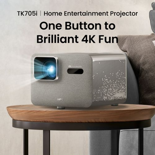 Ein grauer BenQ TK705i 4K-Projektor steht auf einem runden Holztisch. Lichtstrahlen aus der Linse.
