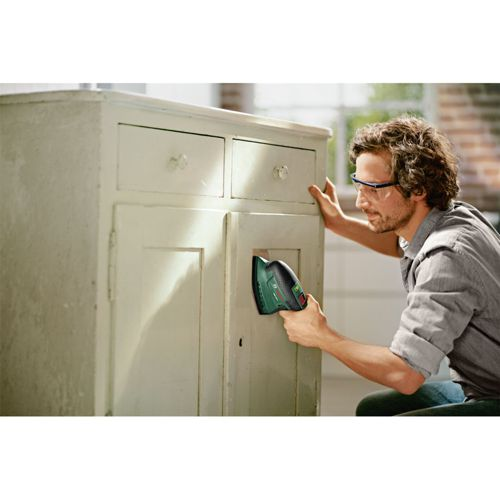 Mann schleift mit einem grünen Gerät an einem alten, hellen Schrank.