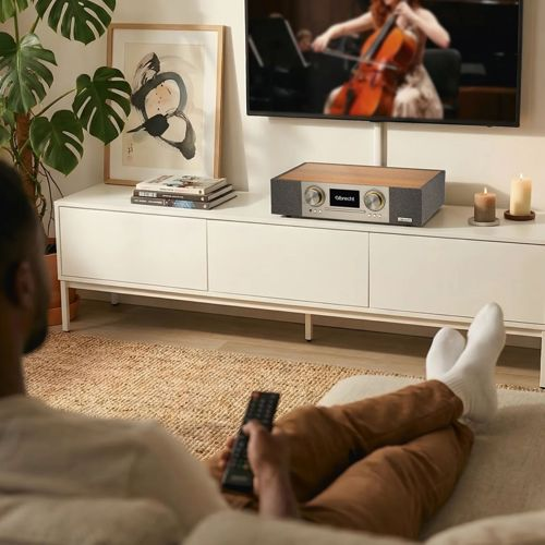 Mann mit Fernbedienung entspannt auf dem Sofa, schaut auf einen Fernseher mit Konzert.