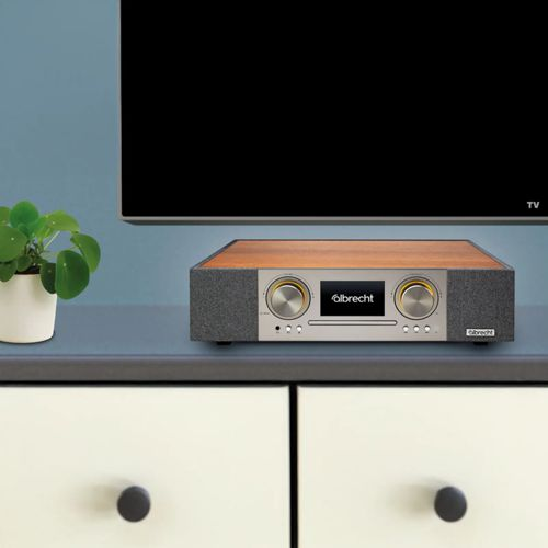 Ein silberner Radioempfänger mit Holzoberseite steht auf einer Kommode unter einem Fernseher.