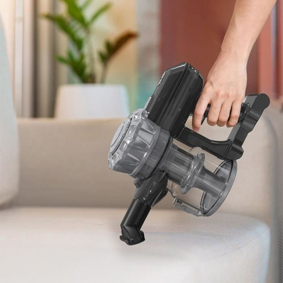Hand hält einen grauen Handstaubsauger über einem hellen Sofa.