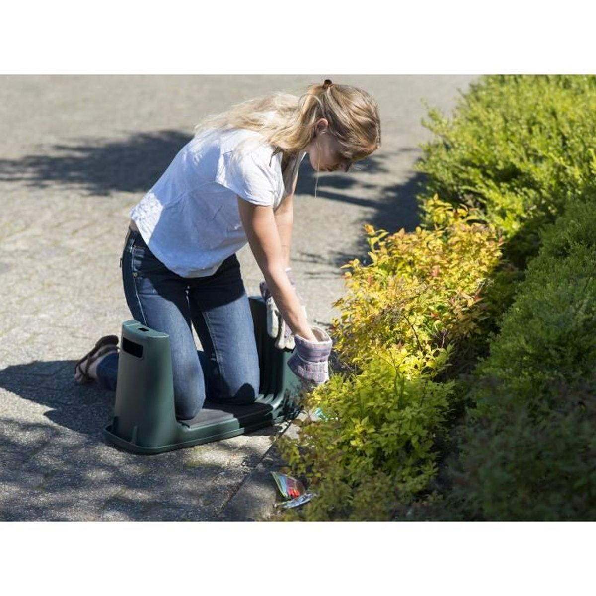 Frau kniet auf einer Gartenbank und arbeitet im Gebüsch.