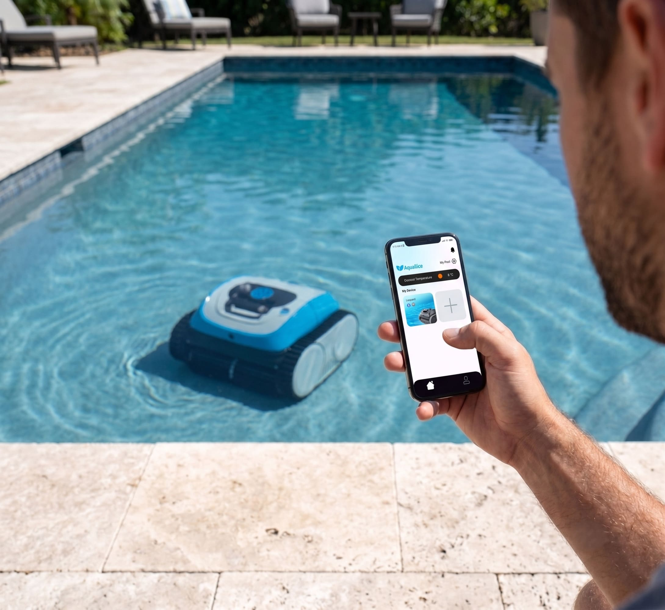 Hombre usa teléfono para controlar limpiador de piscina robot azul en agua. Sillas de piscina atrás.