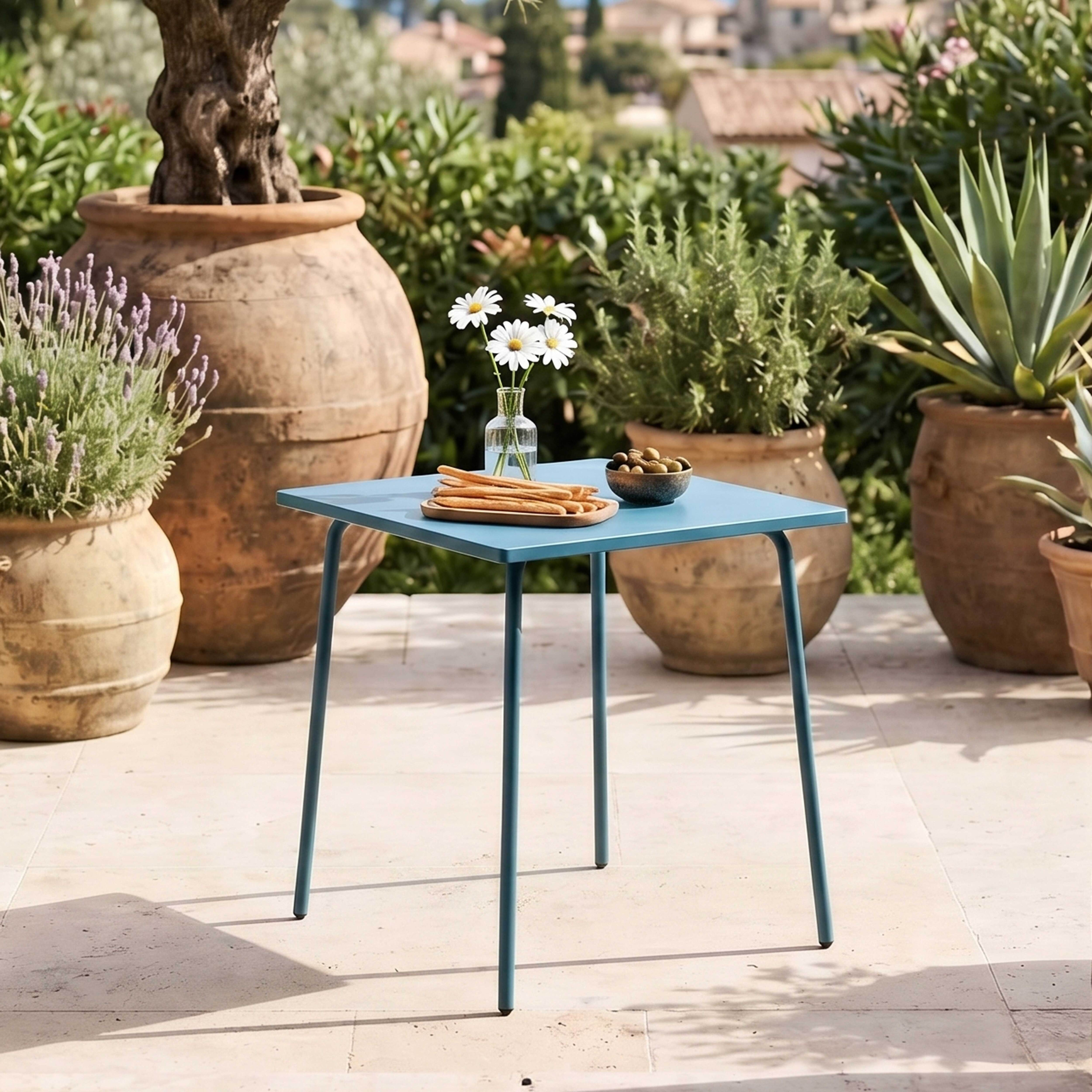Ein blauer Tisch mit Blumen, Oliven und Brot im Freien.