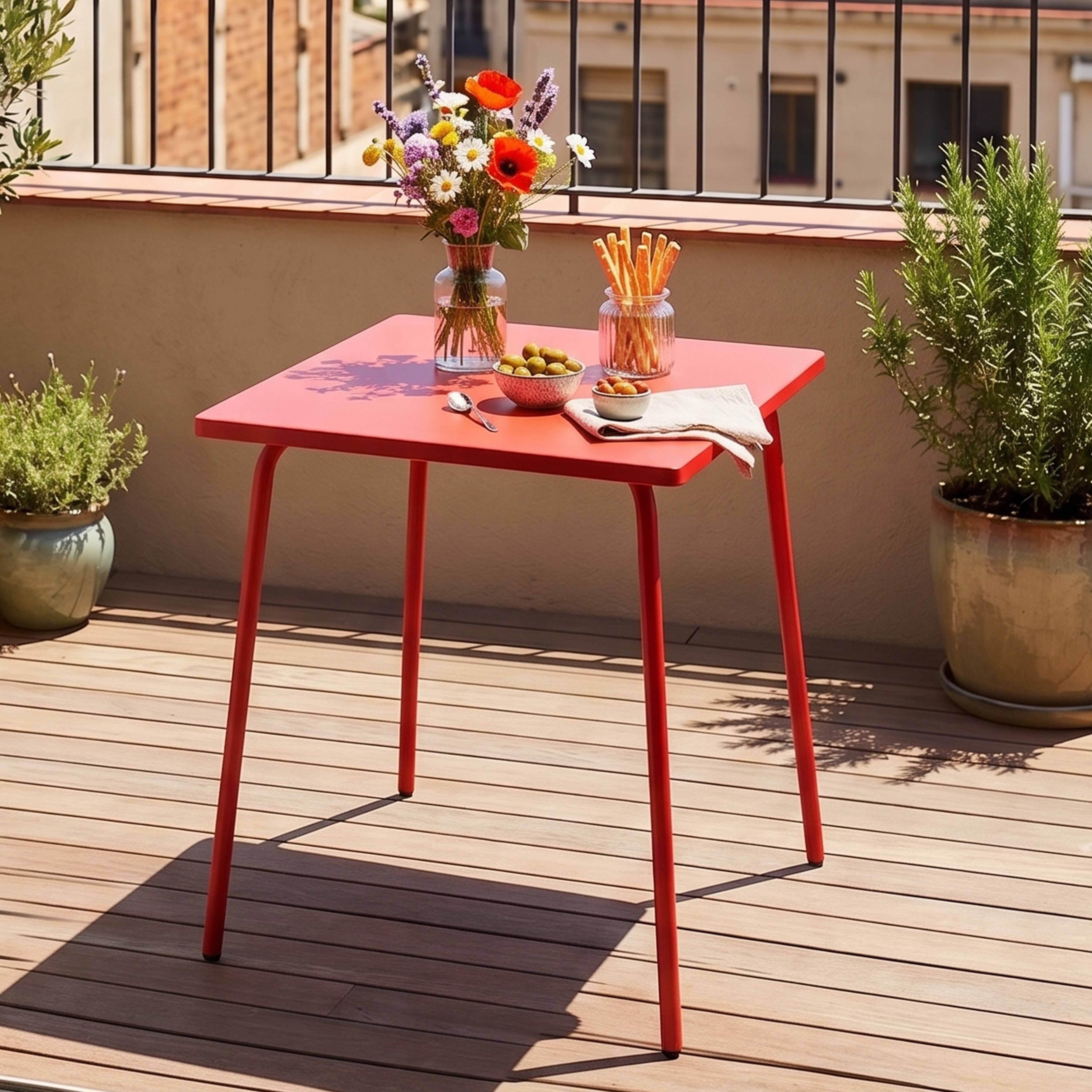 Ein roter Tisch auf einer Holzterrasse mit Blumen, Oliven und Grissini.