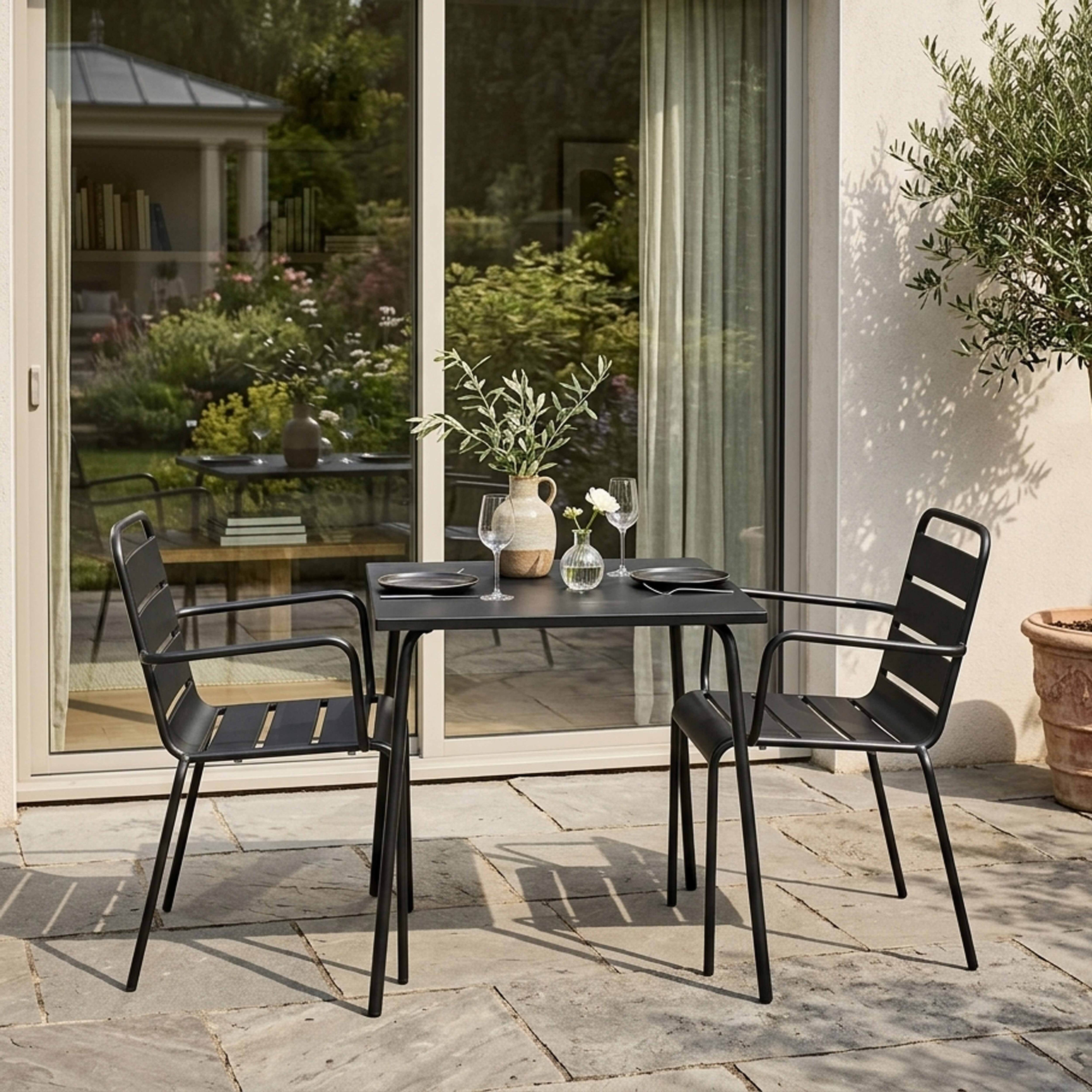 Ein schwarzer Gartentisch mit zwei Stühlen, dekoriert mit einer Vase und Gläsern.