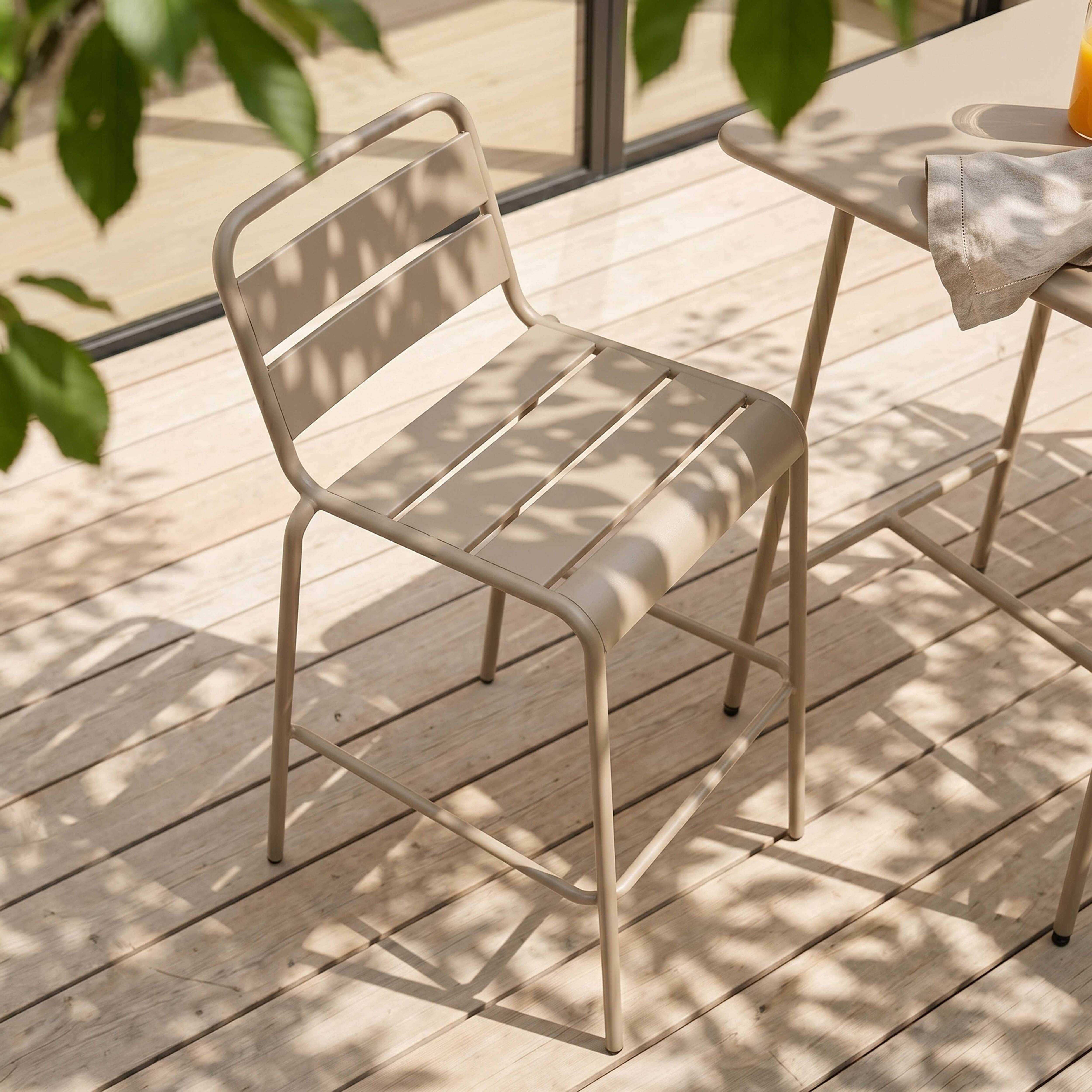 Ein beiger Stuhl und Tisch auf einer Holzterrasse mit Blättern im Schatten.