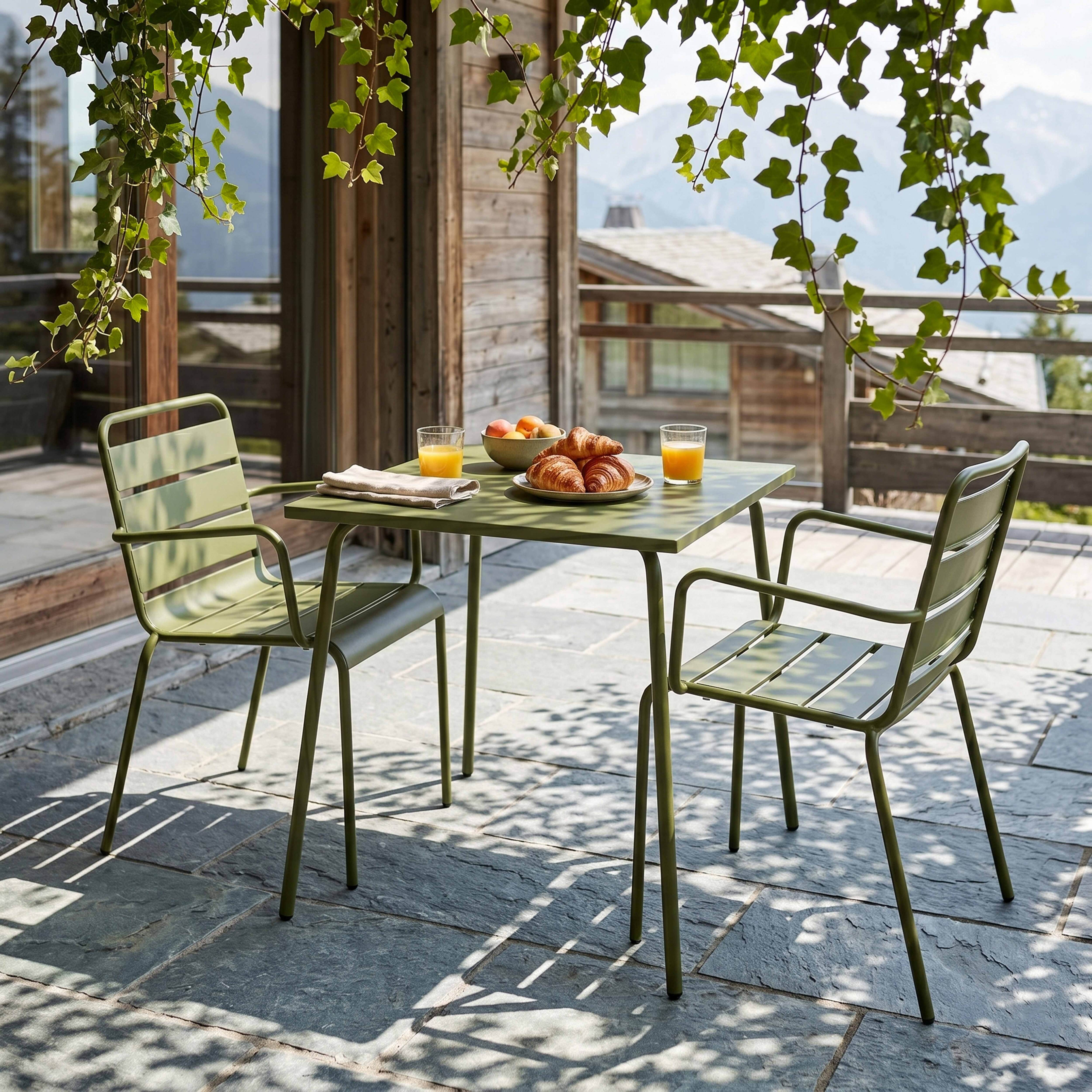 Ein grüner Gartentisch mit zwei Stühlen, Frühstück und Bergen im Hintergrund.