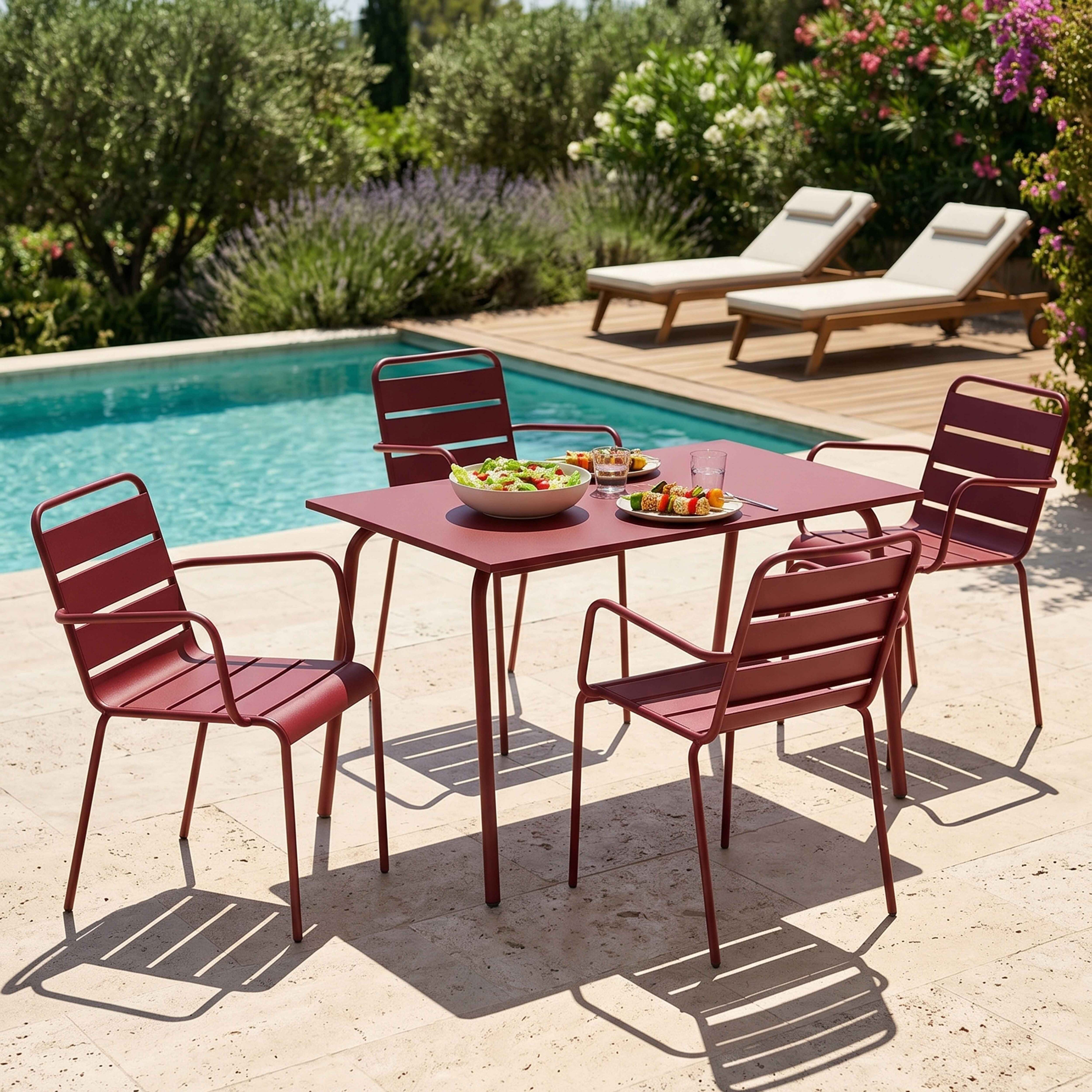 Roter Tisch mit Stühlen am Pool, mit Essen und Liegestühlen im Hintergrund.