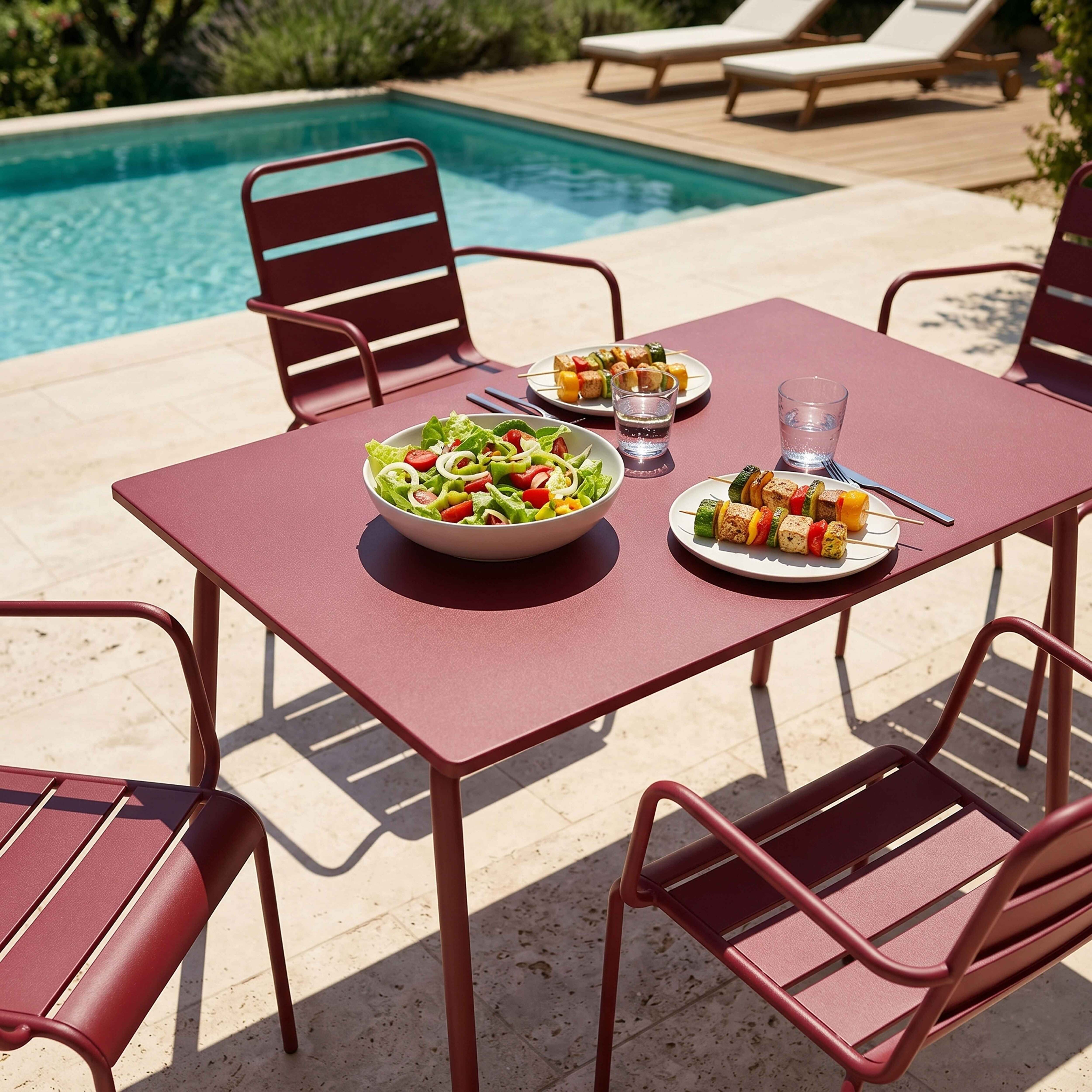 Ein roter Tisch mit Salat und Spießen am Pool.