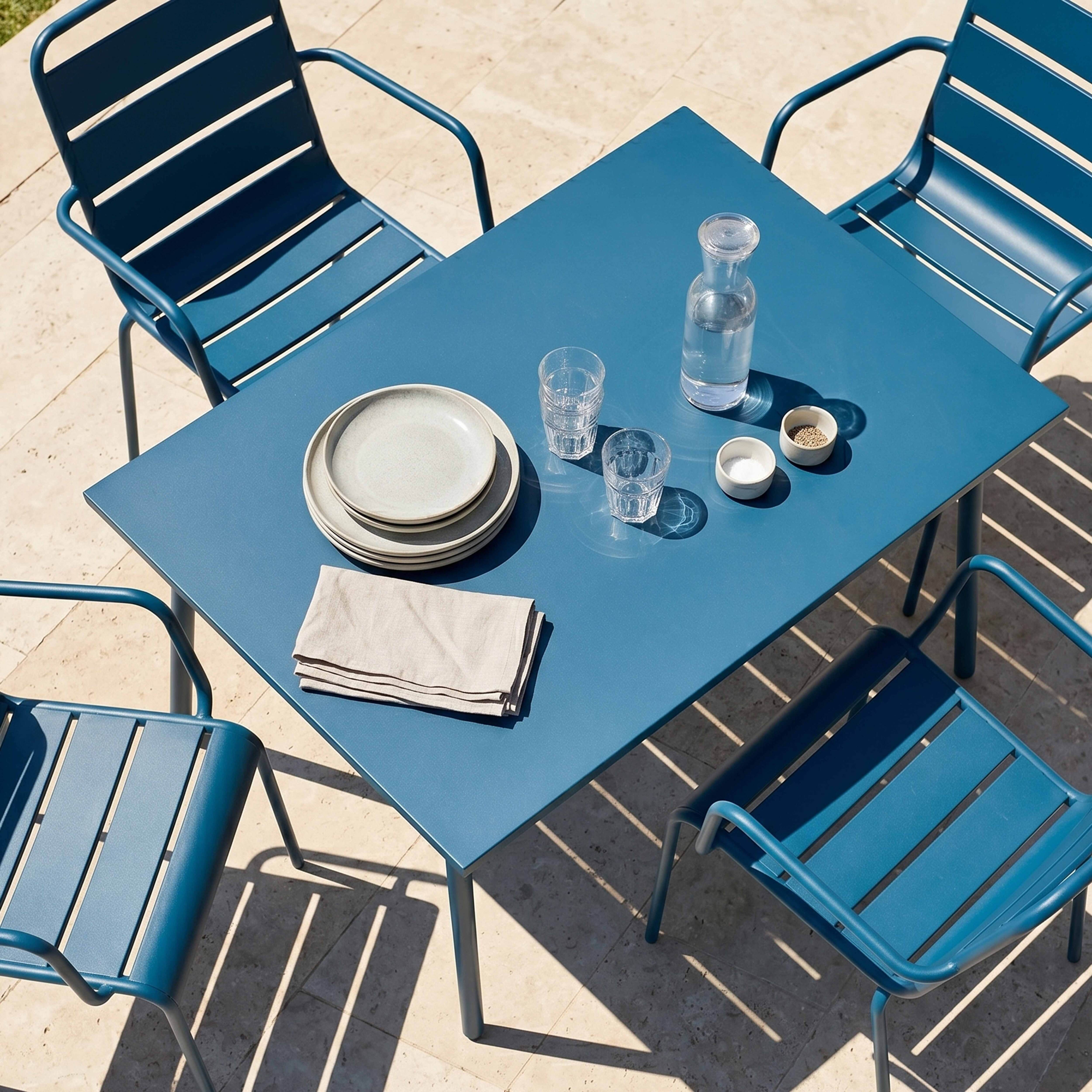 Ein blauer Metalltisch mit vier Stühlen im Freien, gedeckt für eine Mahlzeit.