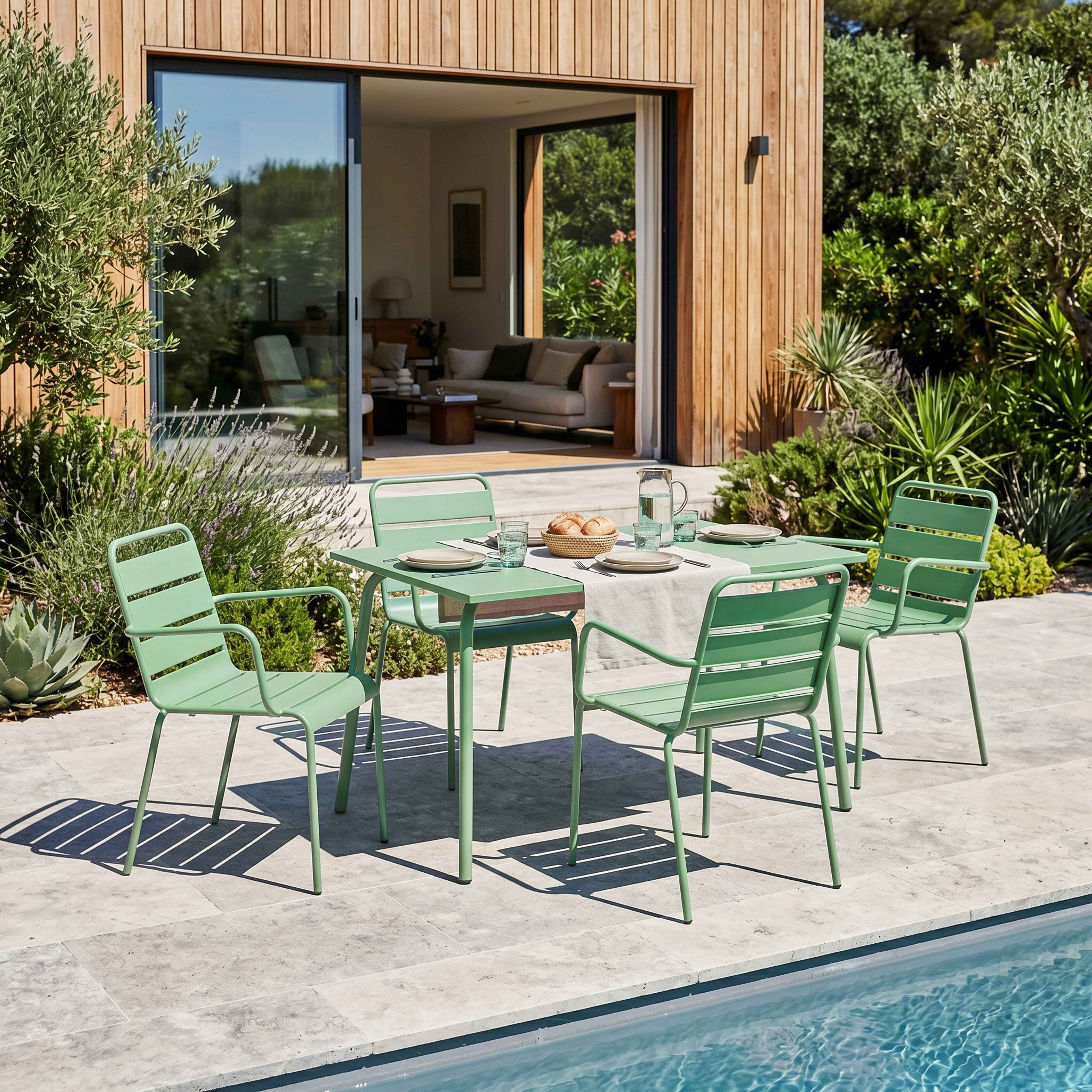Grüne Gartenmöbel stehen auf einer Steinplasterung neben einem Pool.