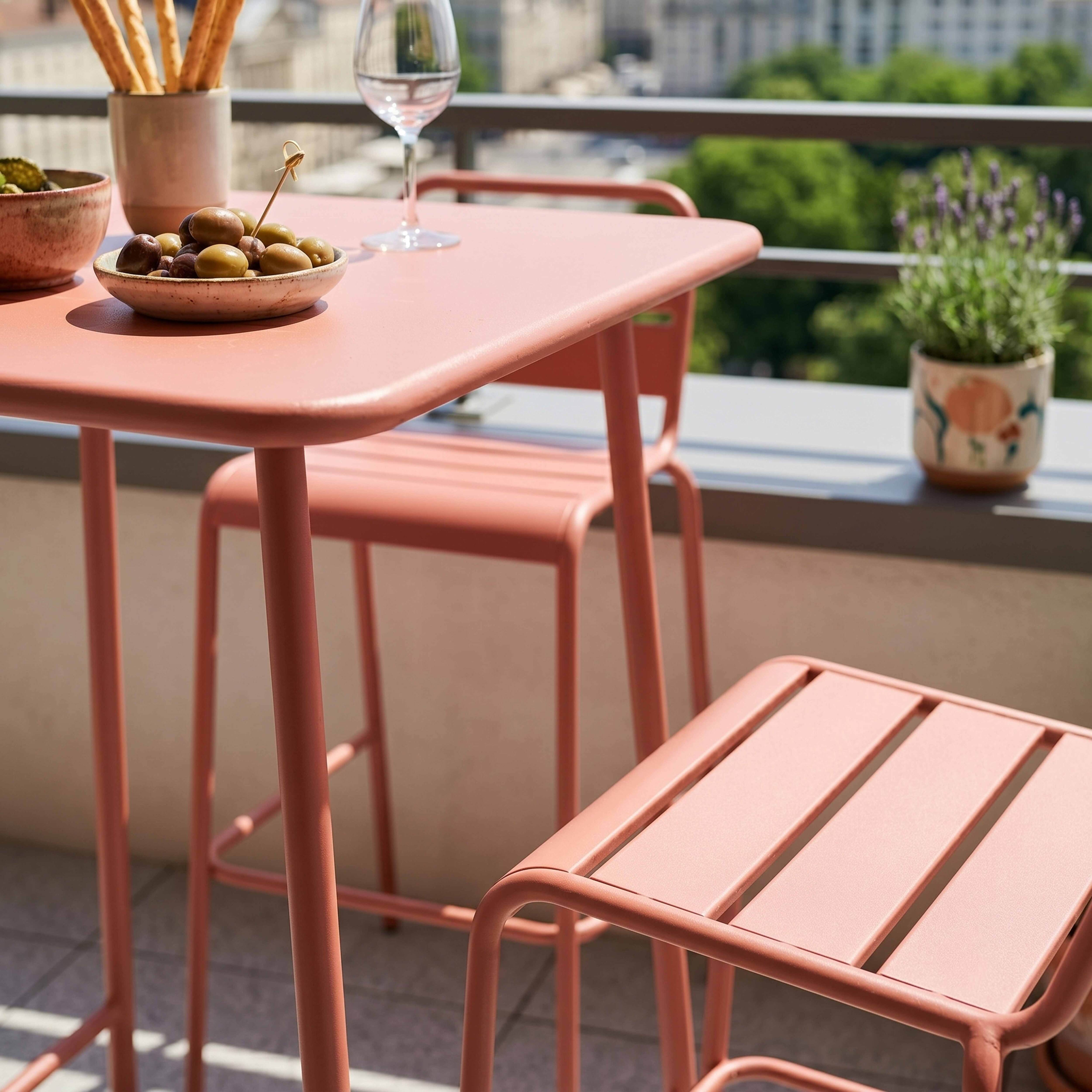 Ein rosafarbener Tisch mit Oliven, Brotstangen und einem Weinglas auf einem Balkon.