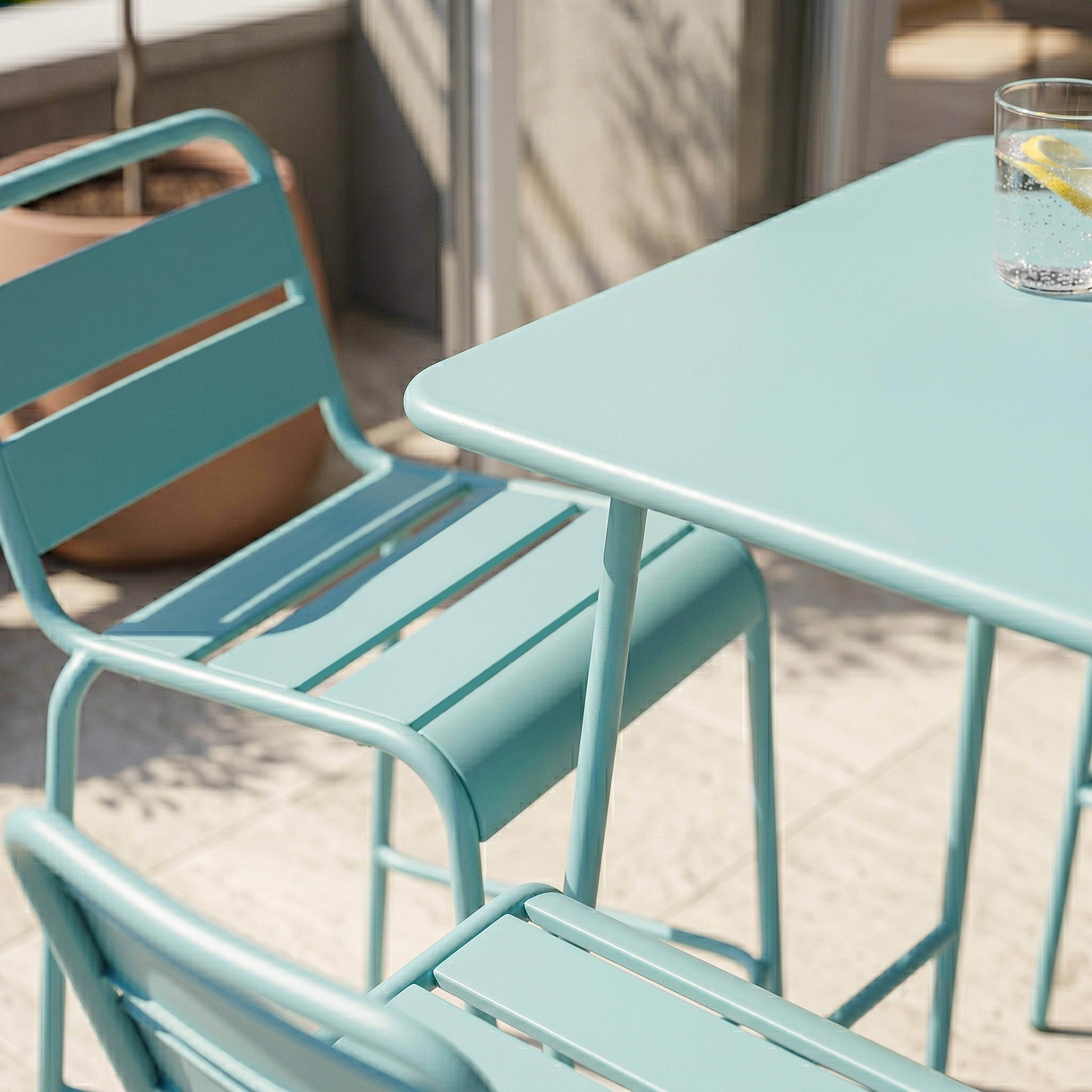 Ein türkisfarbener Tisch und zwei Stühle auf einer Terrasse mit Sonnenschein.