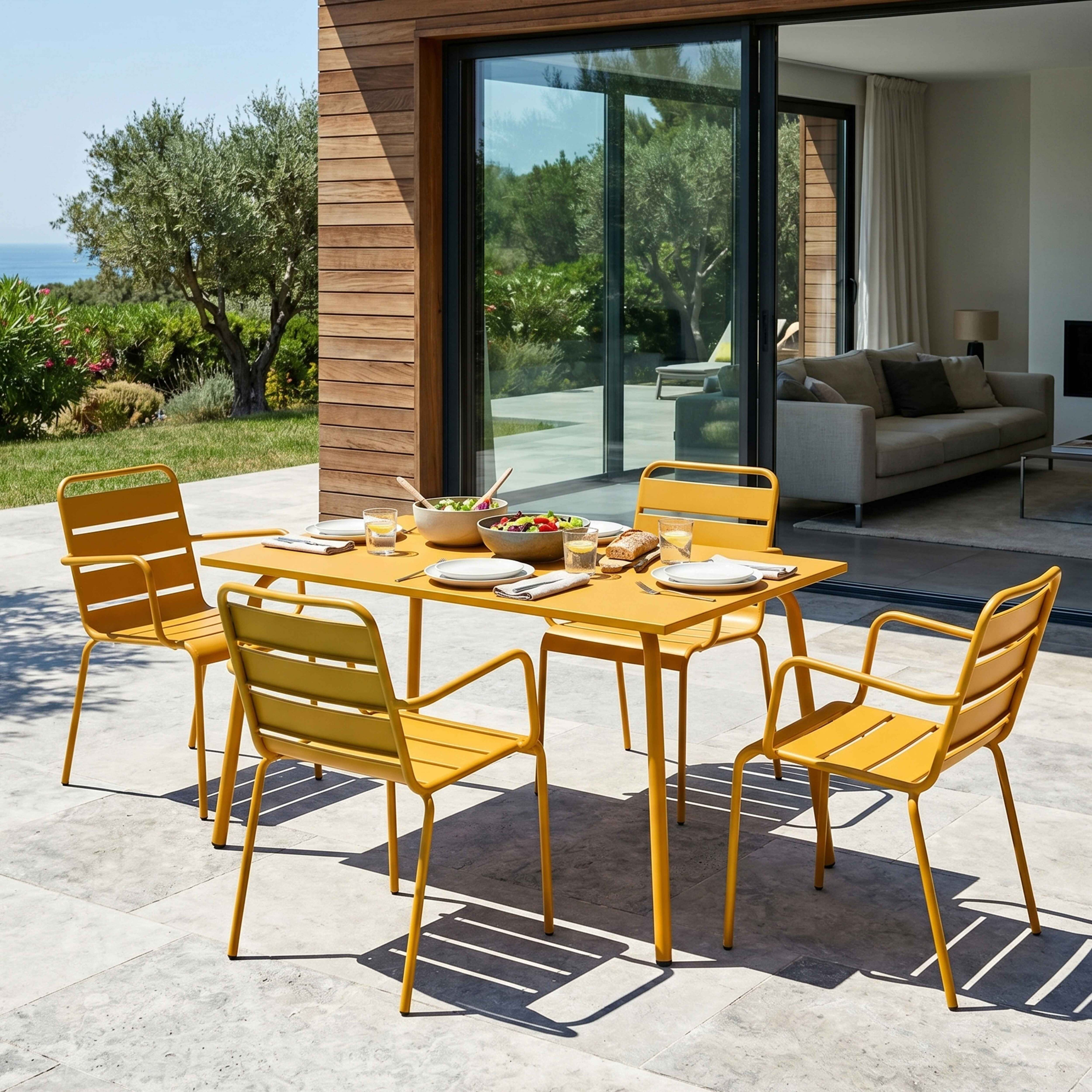 Gelber Gartentisch mit Stühlen, gedeckt mit Salaten und Brot, vor einem Haus.