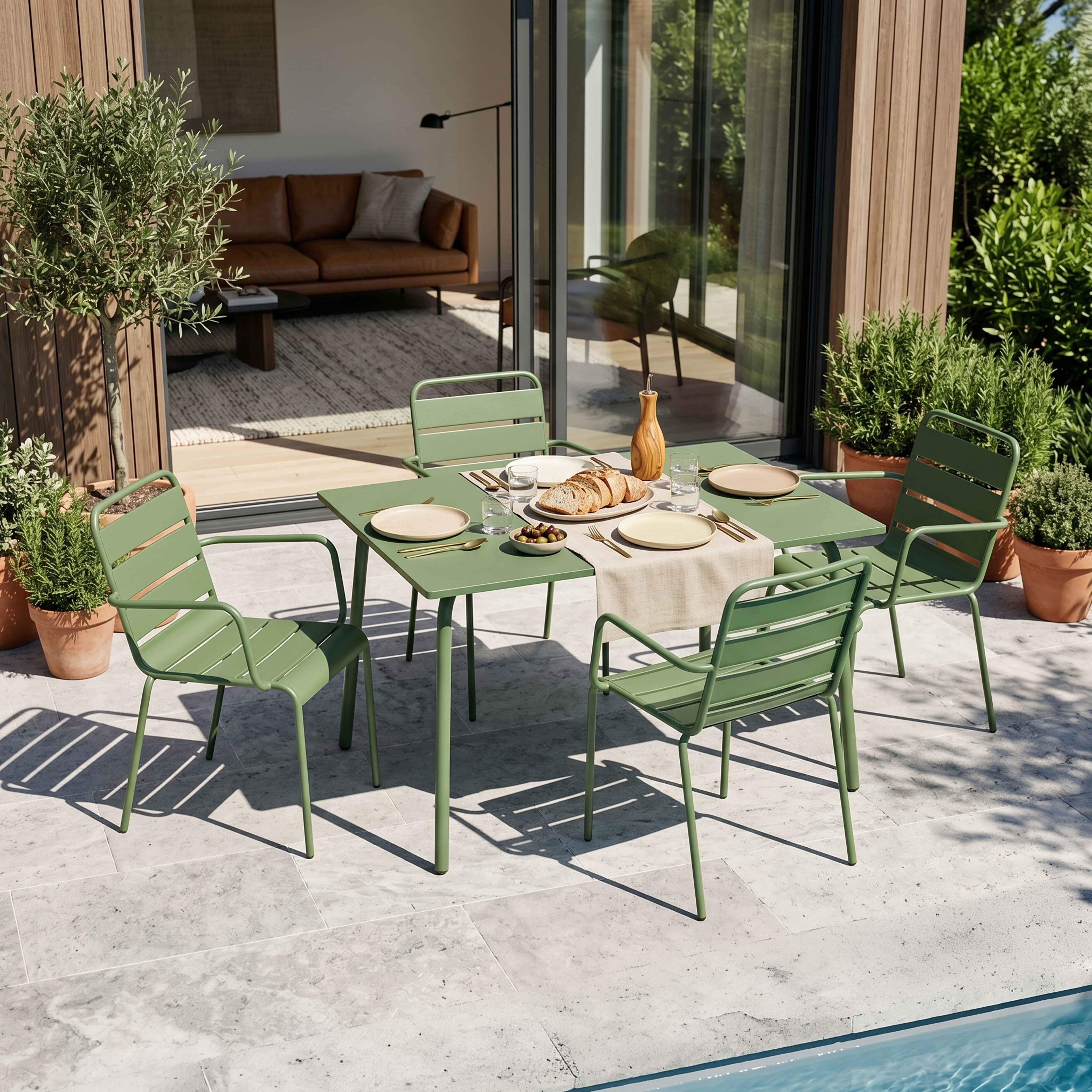 Grüne Metall-Tischgarnitur mit Stühlen auf der Terrasse, neben Pool und Topfpflanzen.