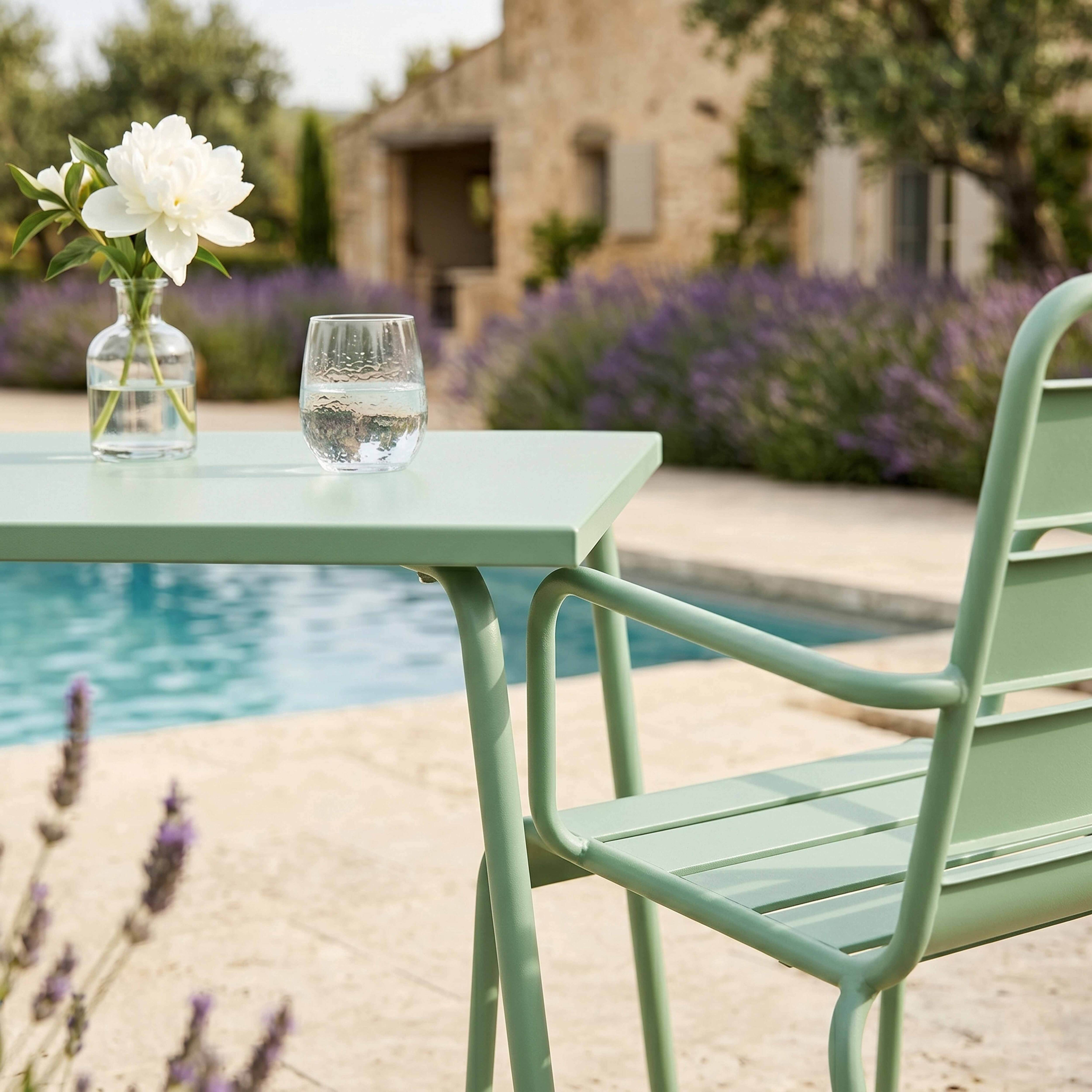 Ein grüner Tisch und Stuhl stehen neben einem Pool mit Blumen und einem Haus.