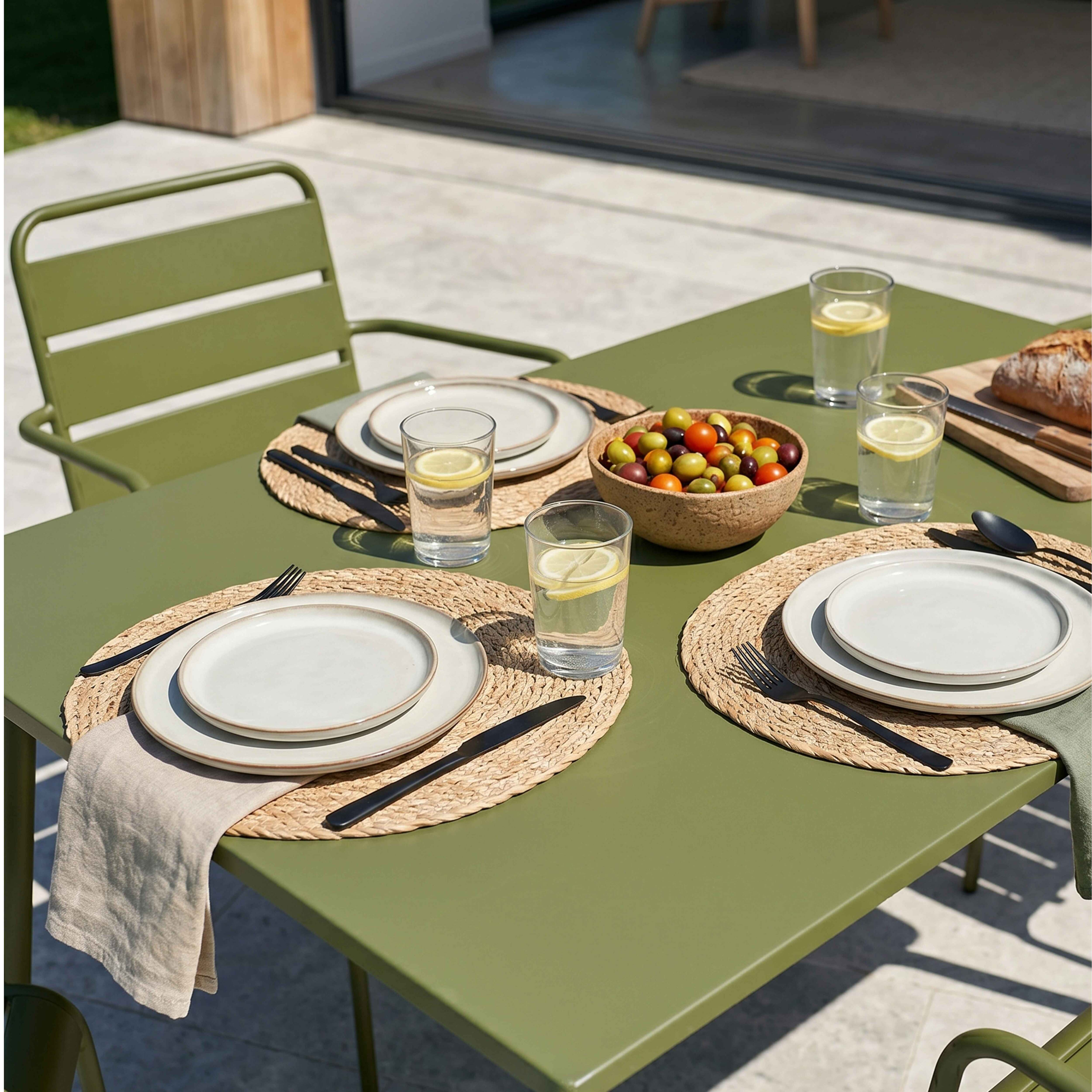 Grüner Gartentisch mit Essgeschirr, Oliven und Brot.