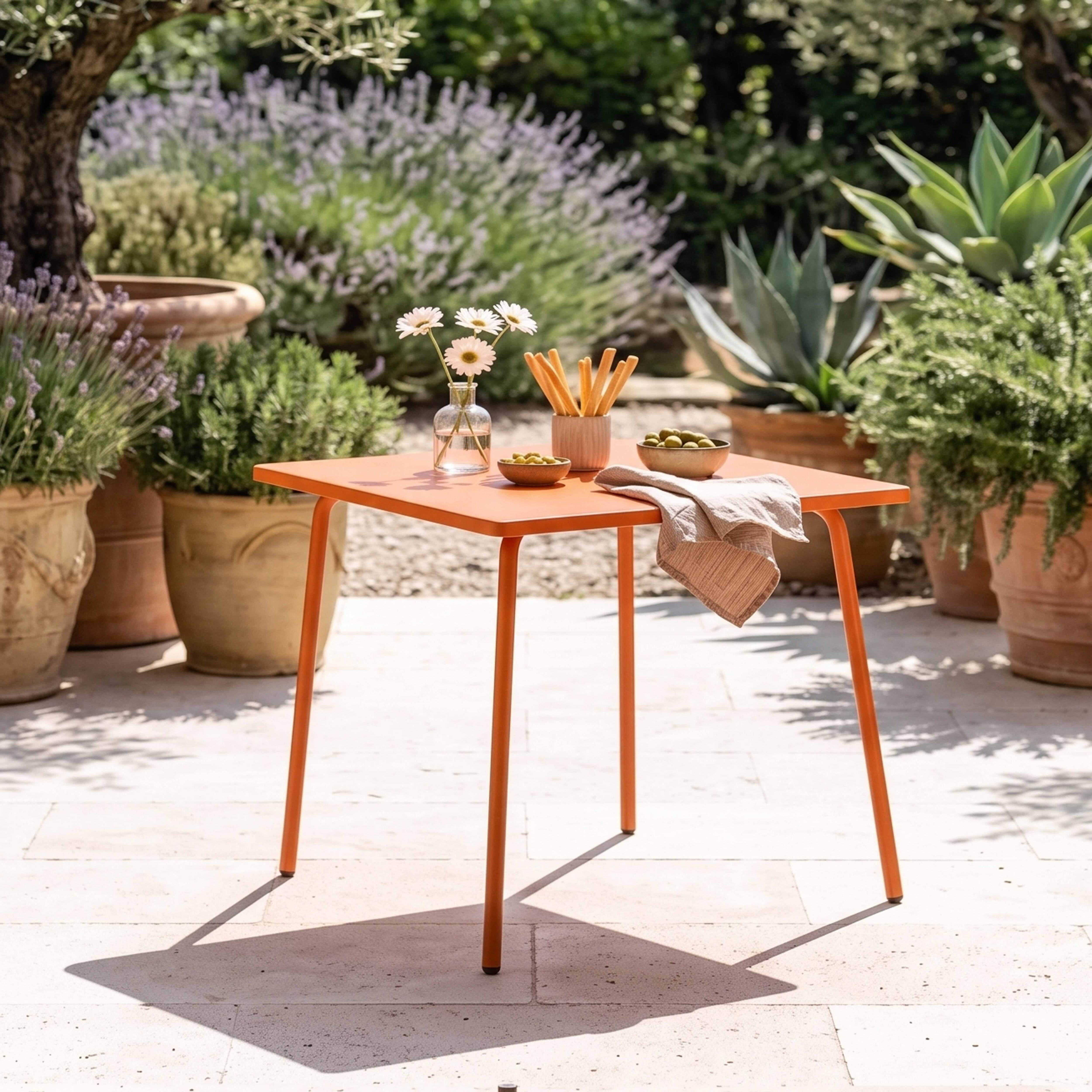 Ein orangefarner Tisch mit Blumen, Grissini und Oliven auf einer Terrasse.