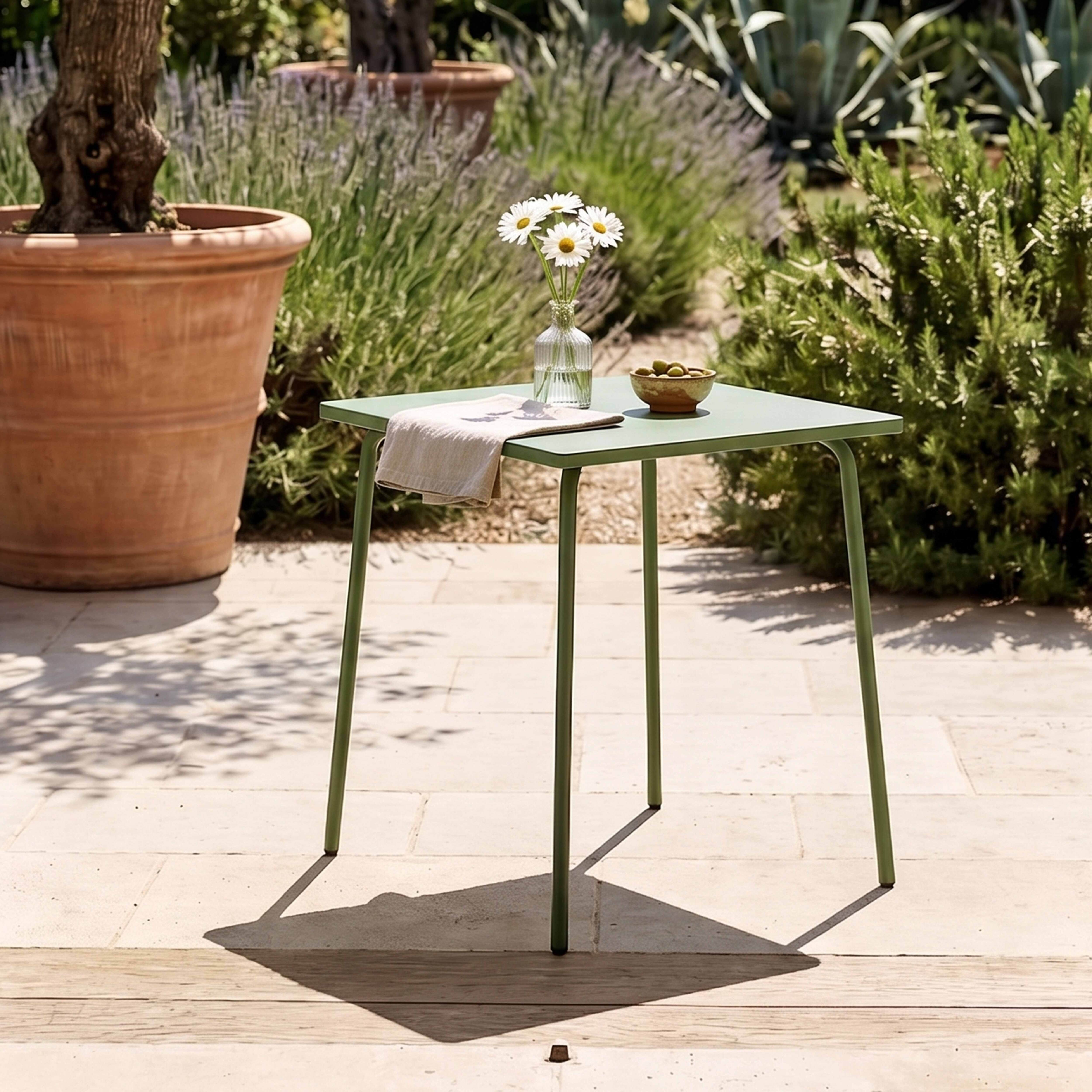 Ein grüner Tisch im Freien mit Blumen, Oliven und einem Tuch.