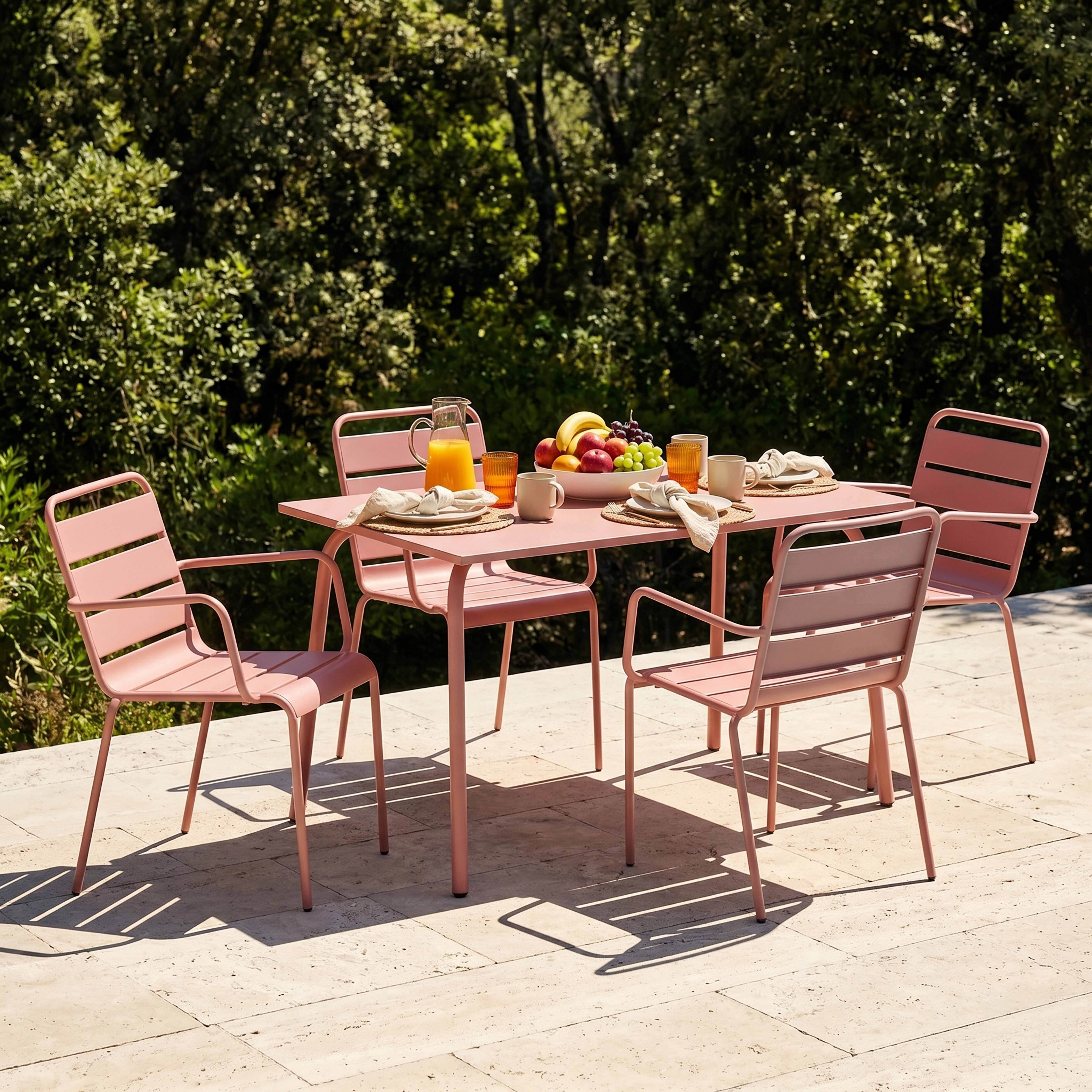 Ein rosafarbener Gartentisch mit vier Stühlen, beladen mit Früchten und Saft.