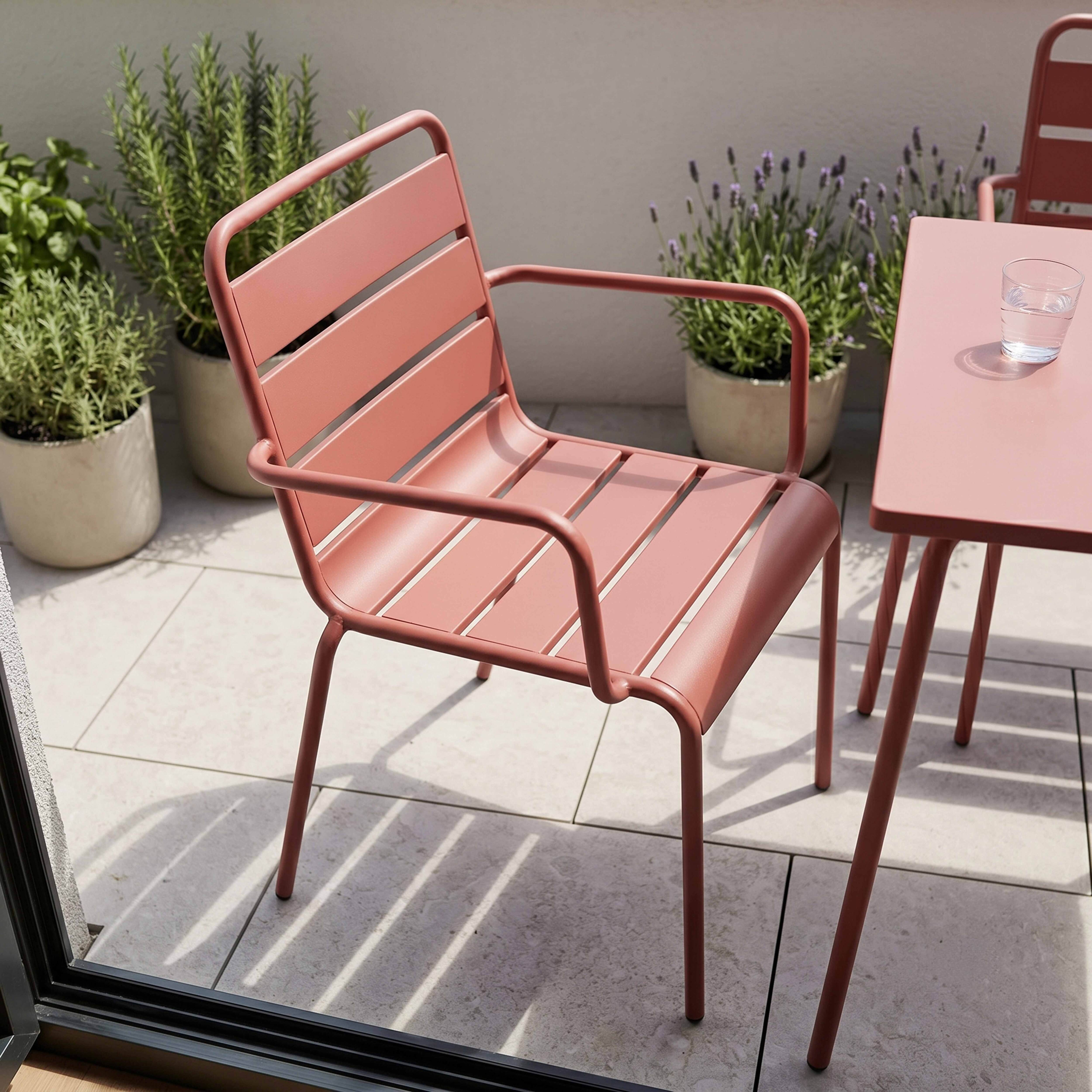Ein korallenroter Stuhl und Tisch stehen auf einer gefliesten Terrasse mit Pflanzen.