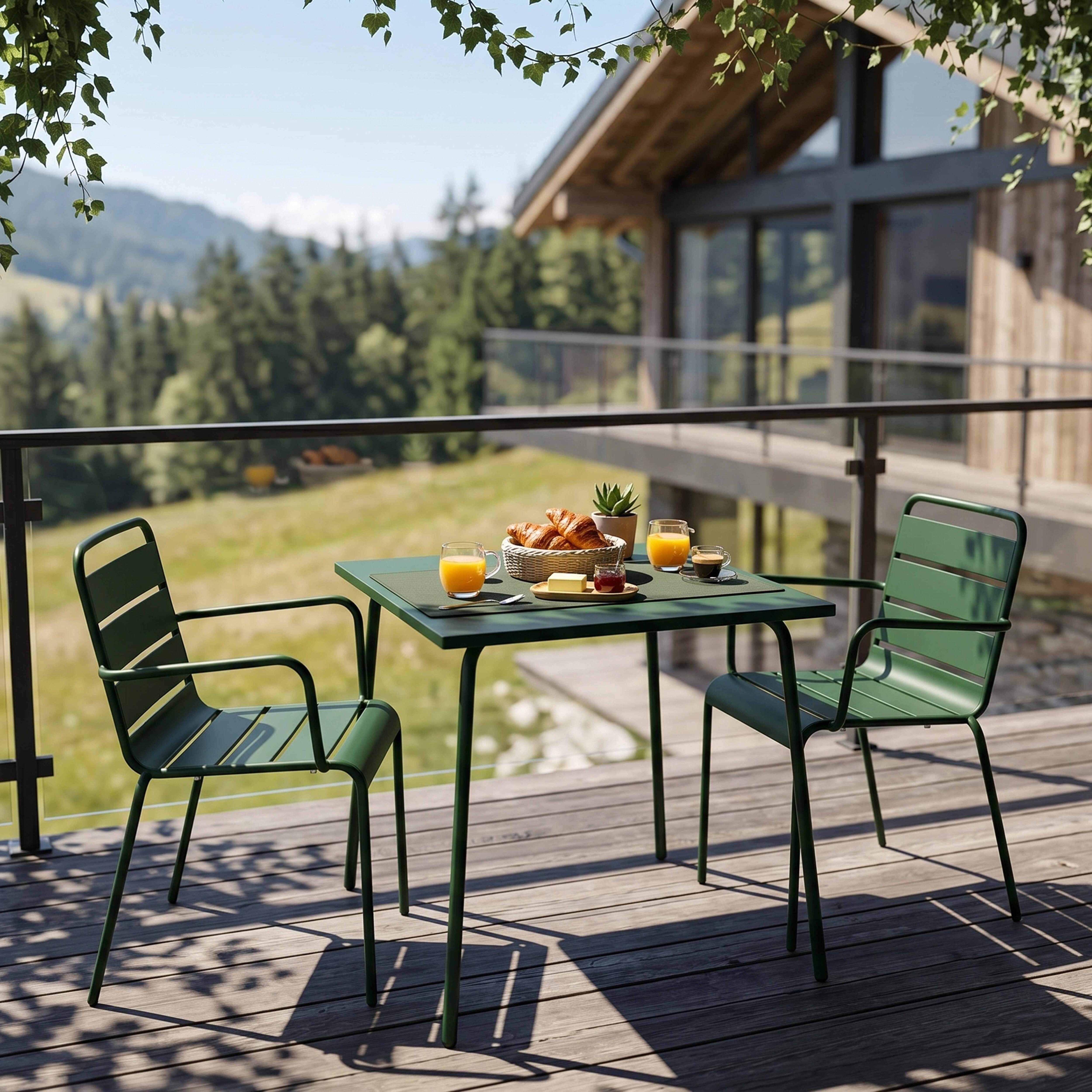 Grüner Gartentisch mit zwei Stühlen und Frühstück auf einer Holzterrasse.
