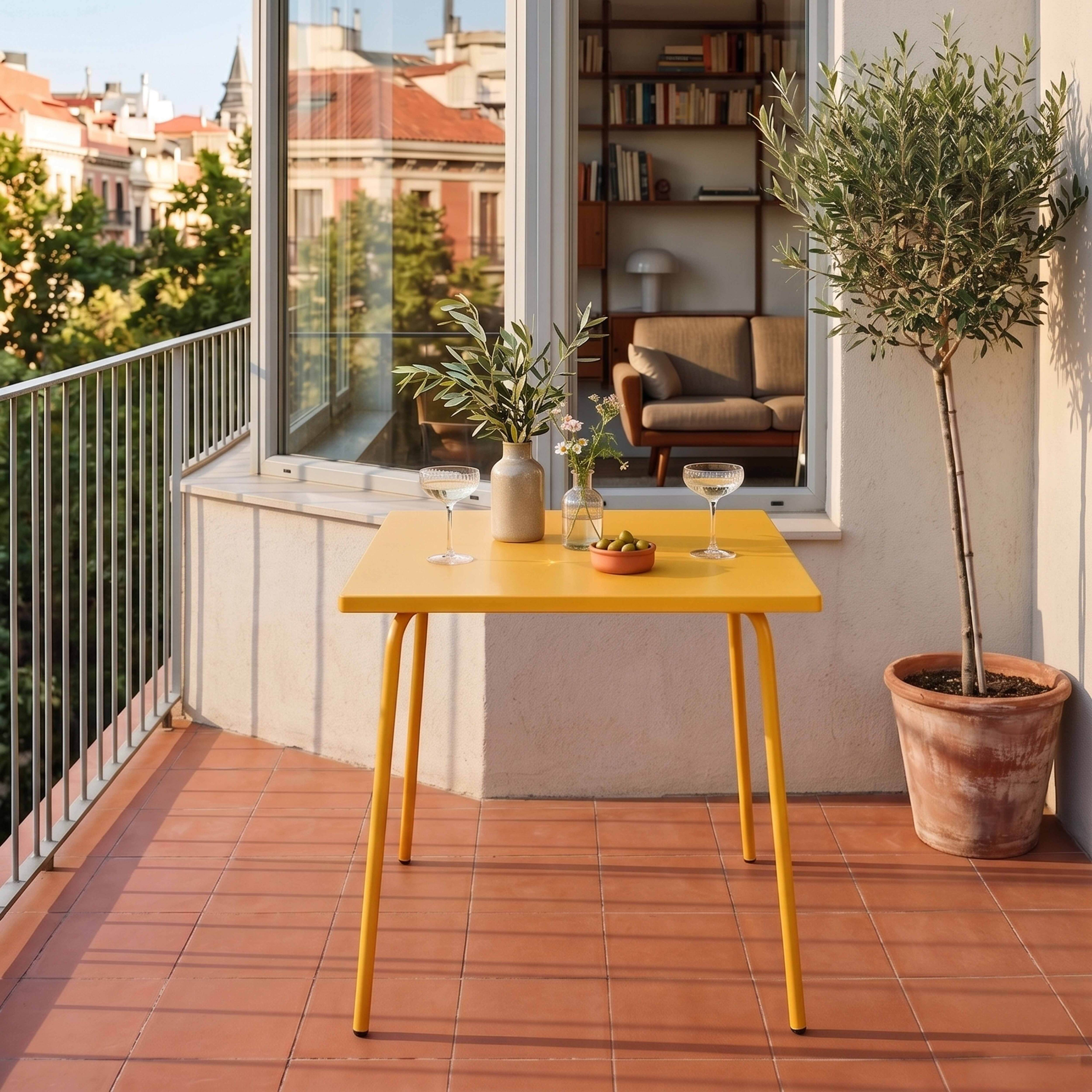Gelber Tisch auf einem Balkon mit Terrakotta-Fliesen, Blick auf Gebäude.