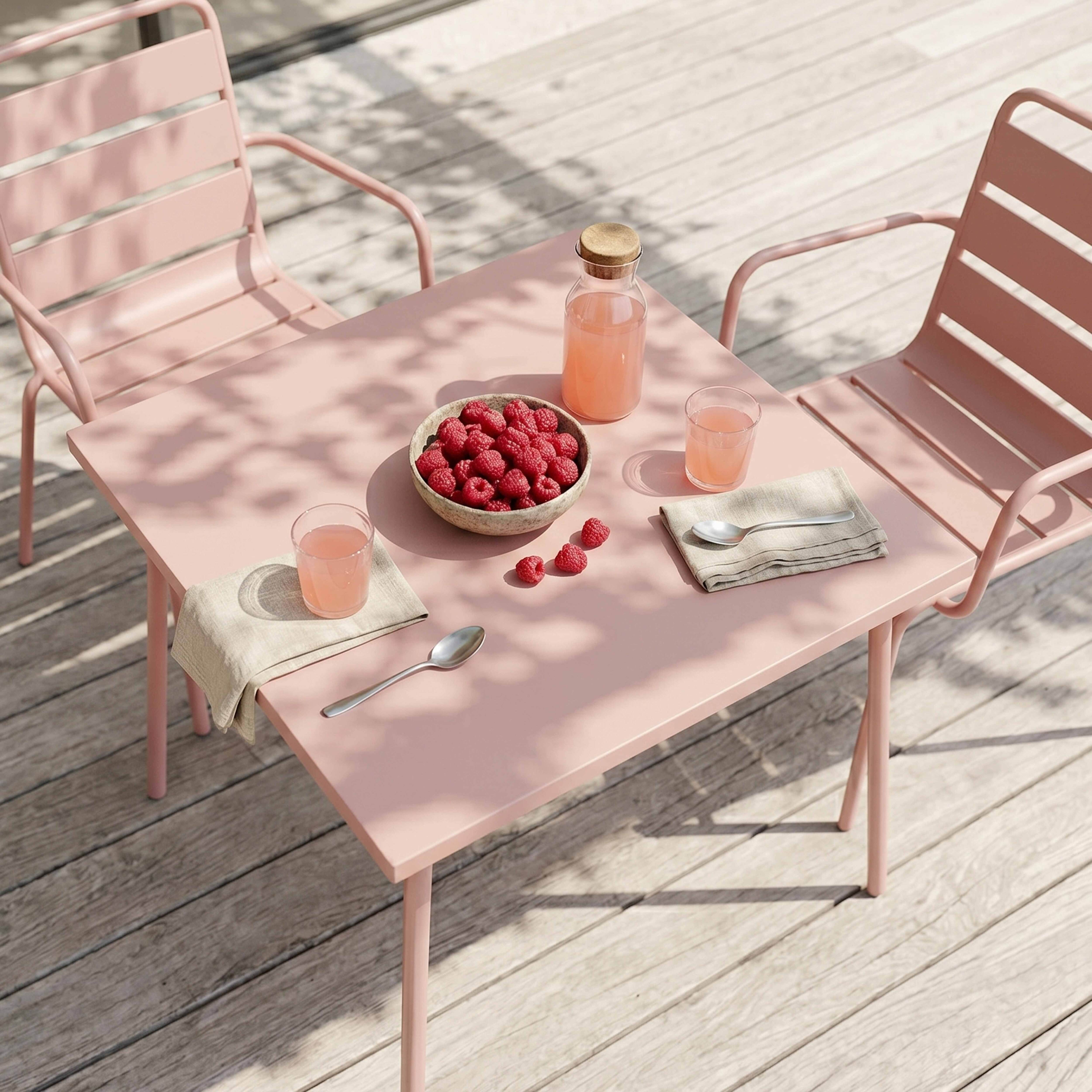 Ein rosafarbener Tisch mit zwei Stühlen, Beeren und Saft im Freien.