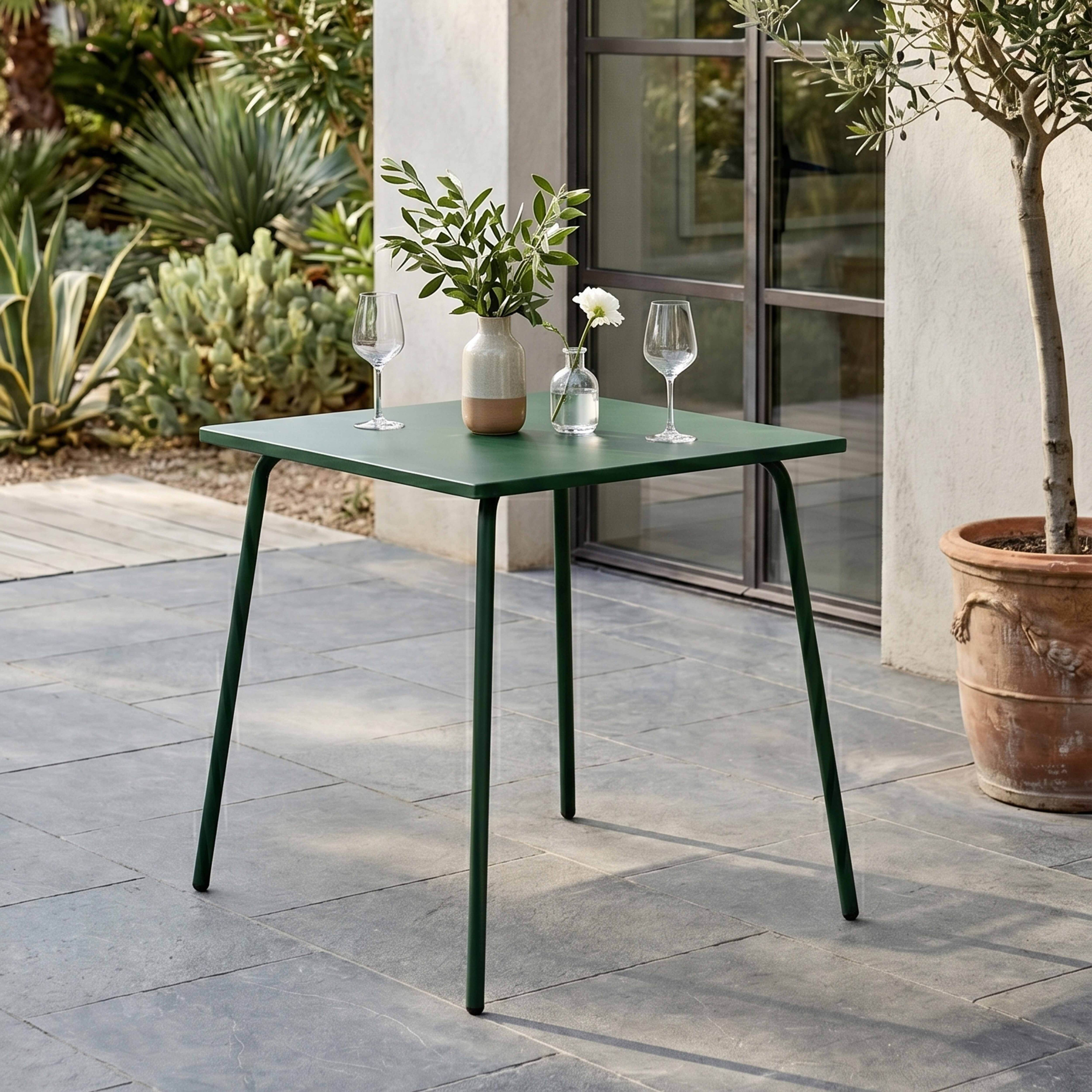 Grüner Gartentisch mit zwei Gläsern und Vase mit Zweigen.