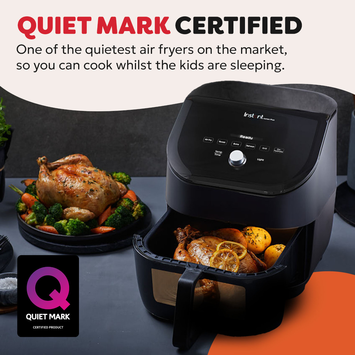 A black air fryer with roasted chicken and vegetables, Quiet Mark logo.